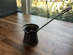 An ibrik is used to make Turkish coffee. Water is heated inside the ibrik, coffee grounds are then added, and a spoon is used to stir and help with brewing.